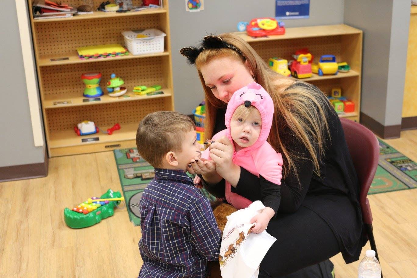 Person in cat ears holding a child in a pink costume, looking at another child