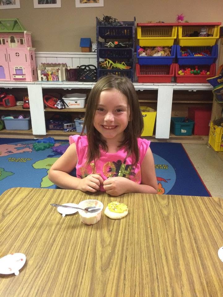 Child sitting at a table with a small cup and cookie in a classroom
