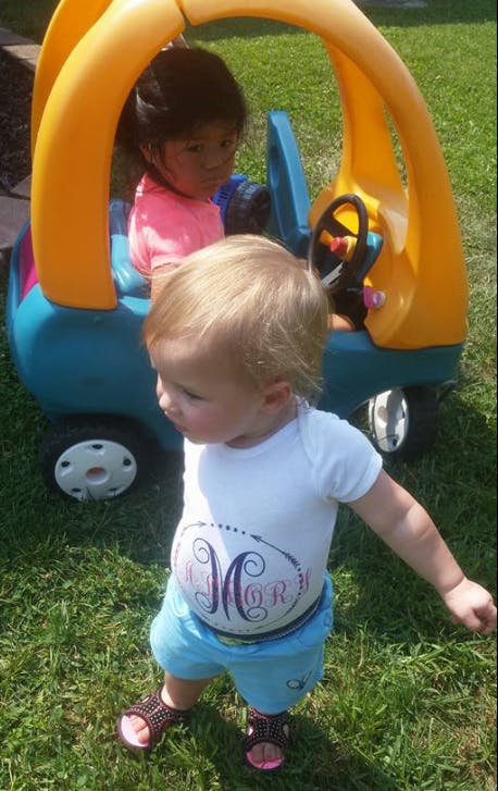 Child in a toy car and another child standing in grass