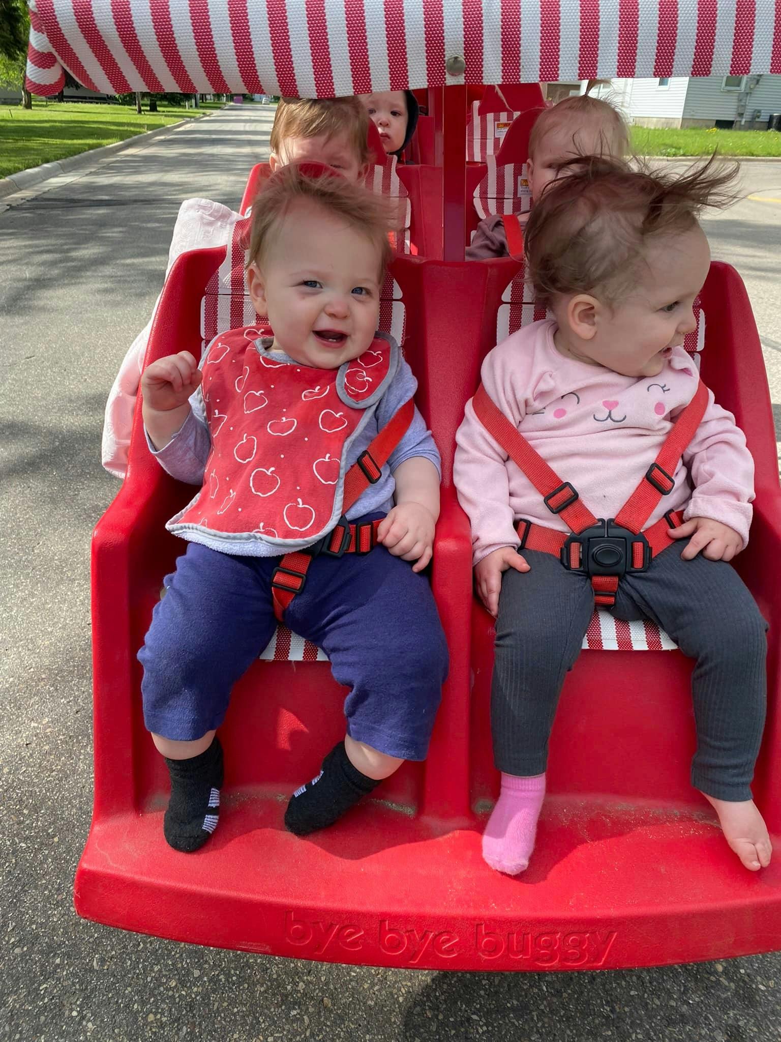 Two children in a red multi-seat stroller