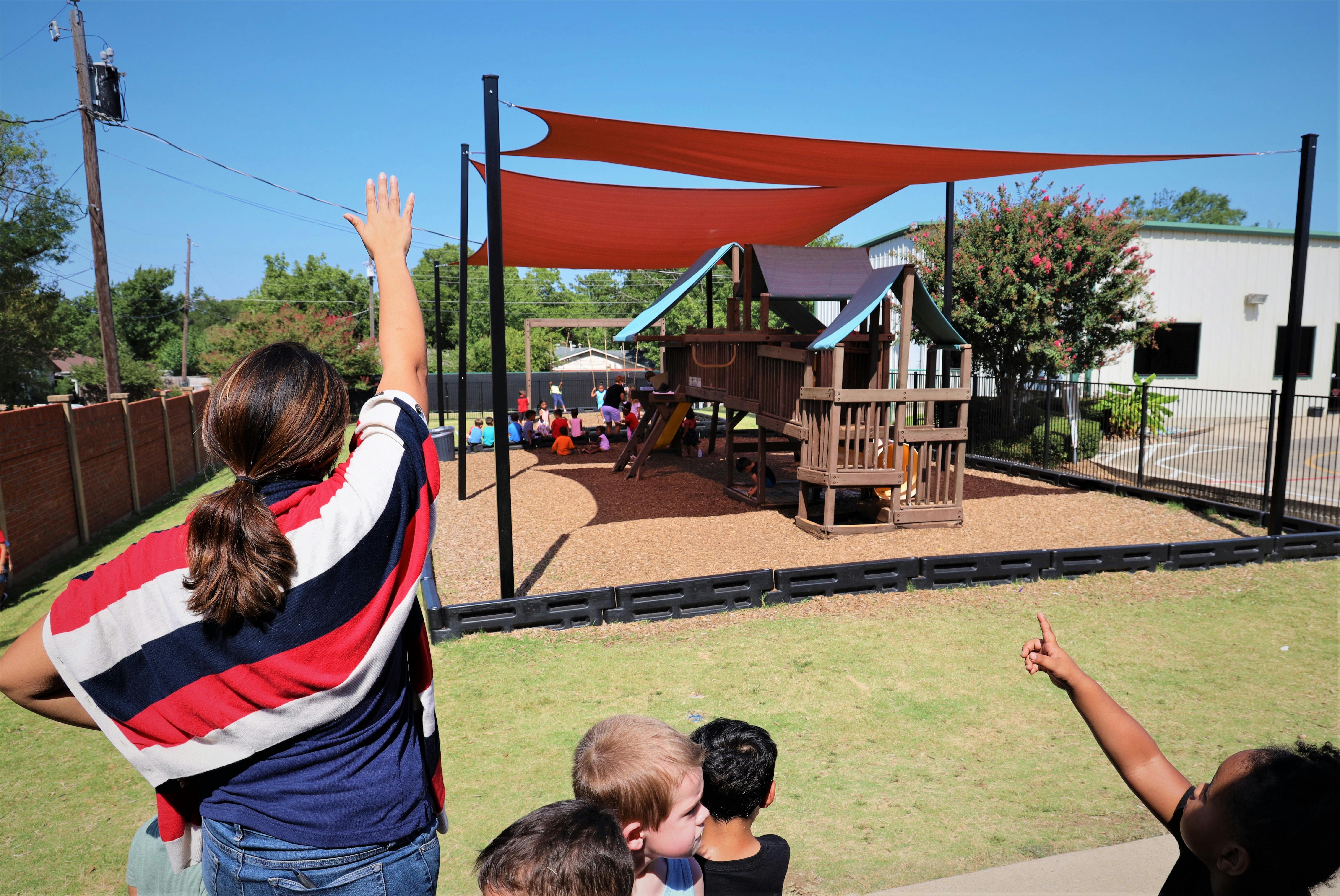Person with arm raised looking at children on a playground