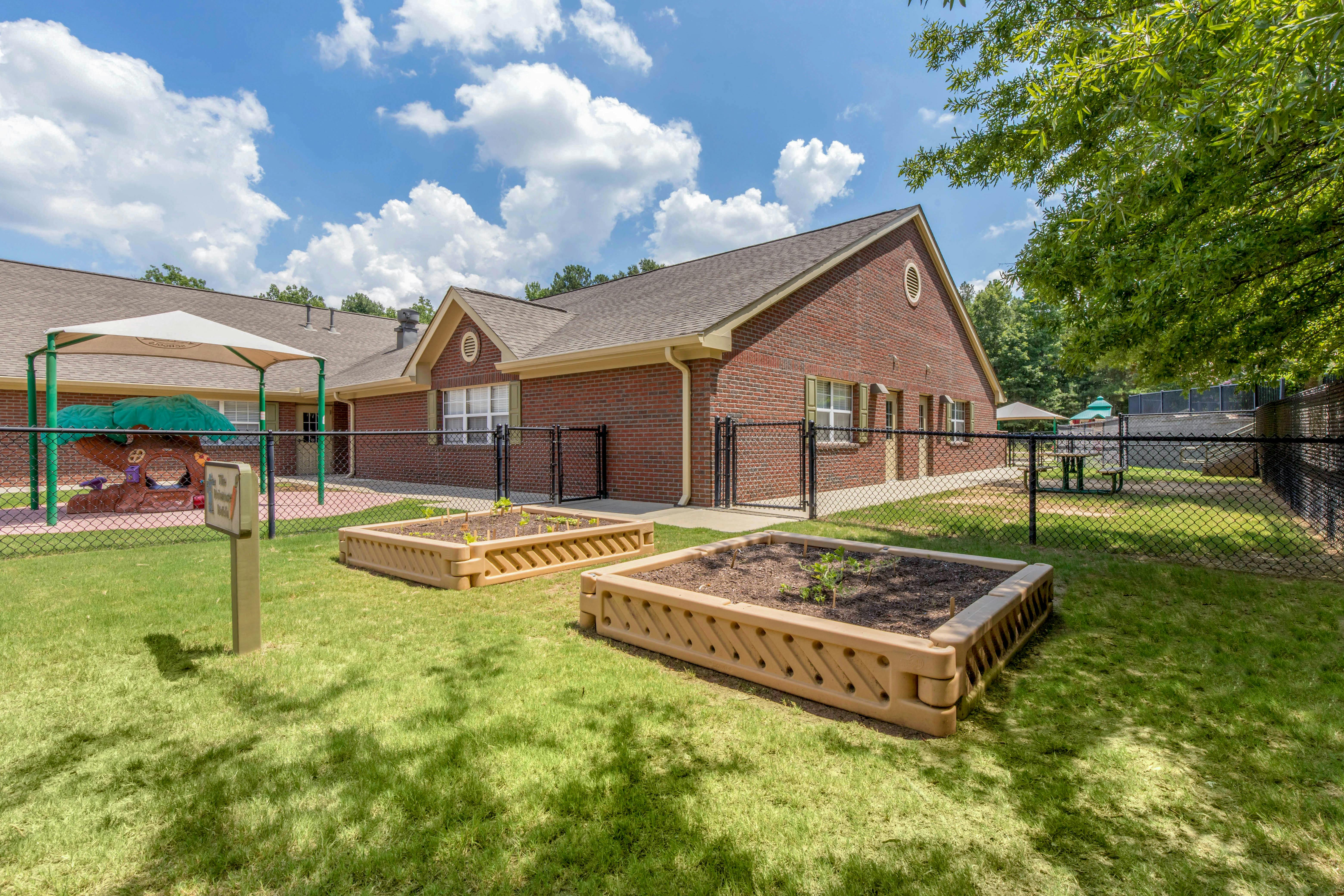 Fenced playground area next to a brick building, with raised garden beds