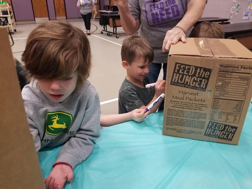 Two children and an adult with a "Feed the Hunger" box