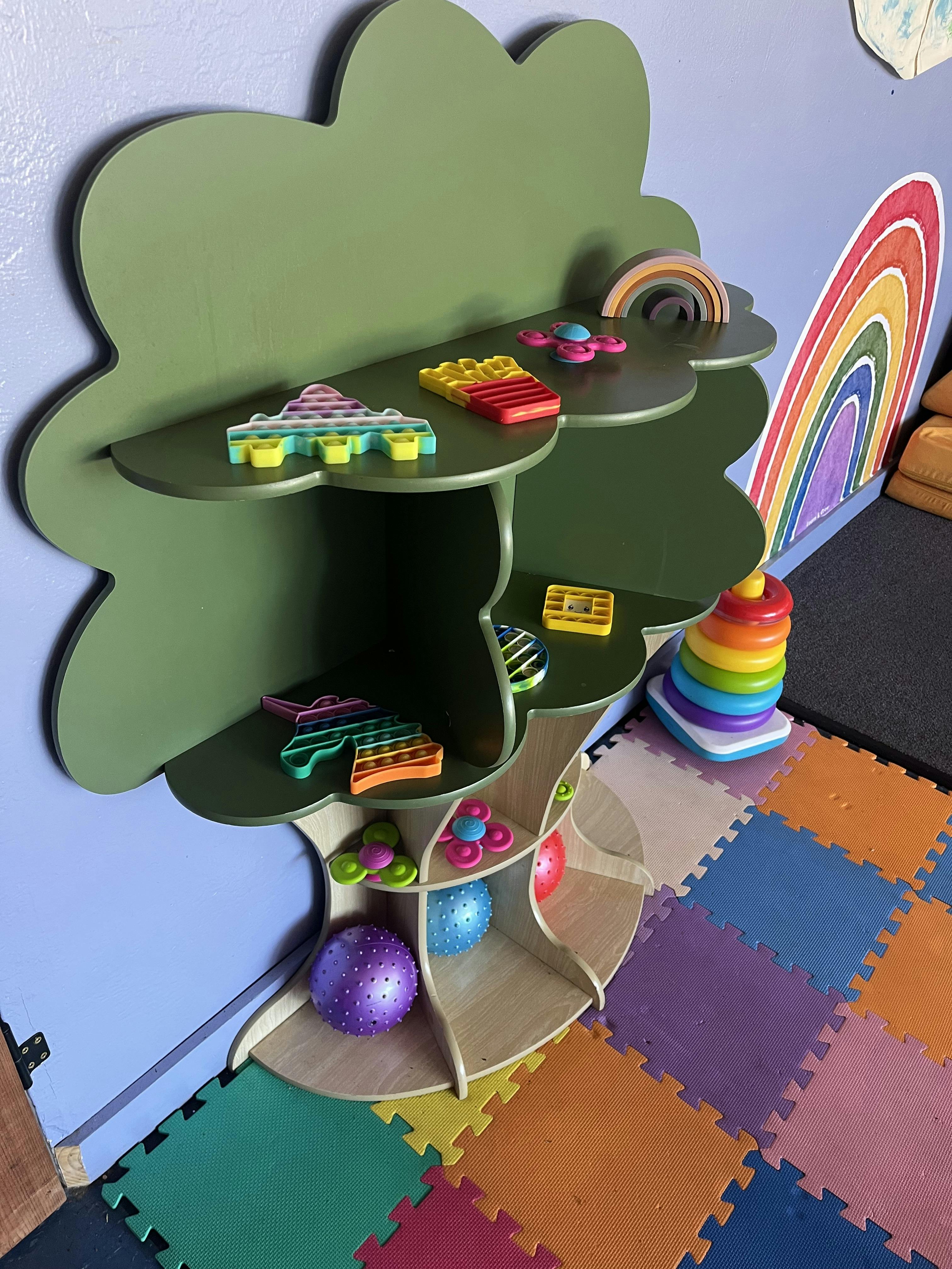 Tree-shaped green wooden shelf filled with colorful toys and pop-its