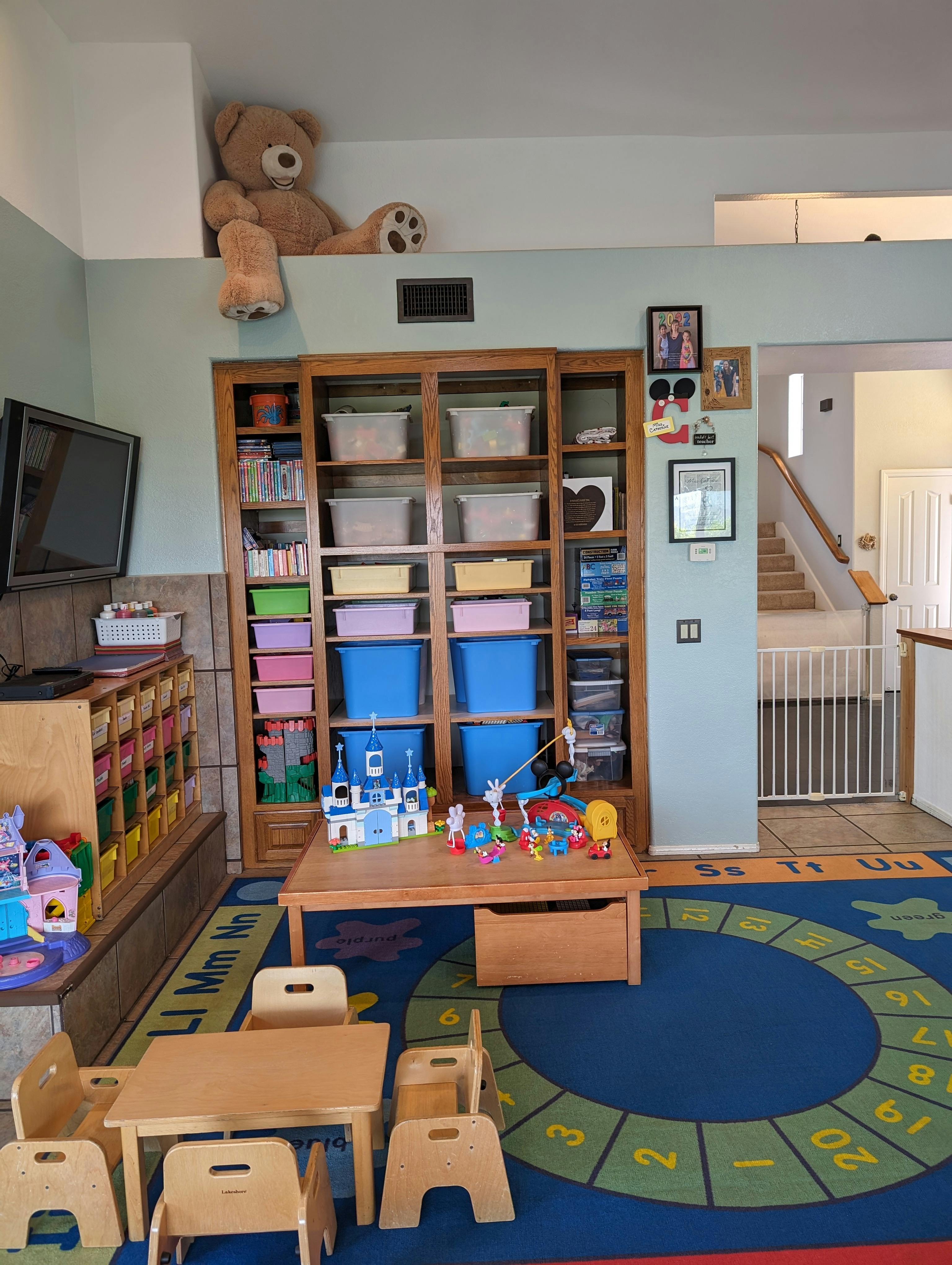 Playroom with small tables and chairs, toy storage, and a large teddy bear