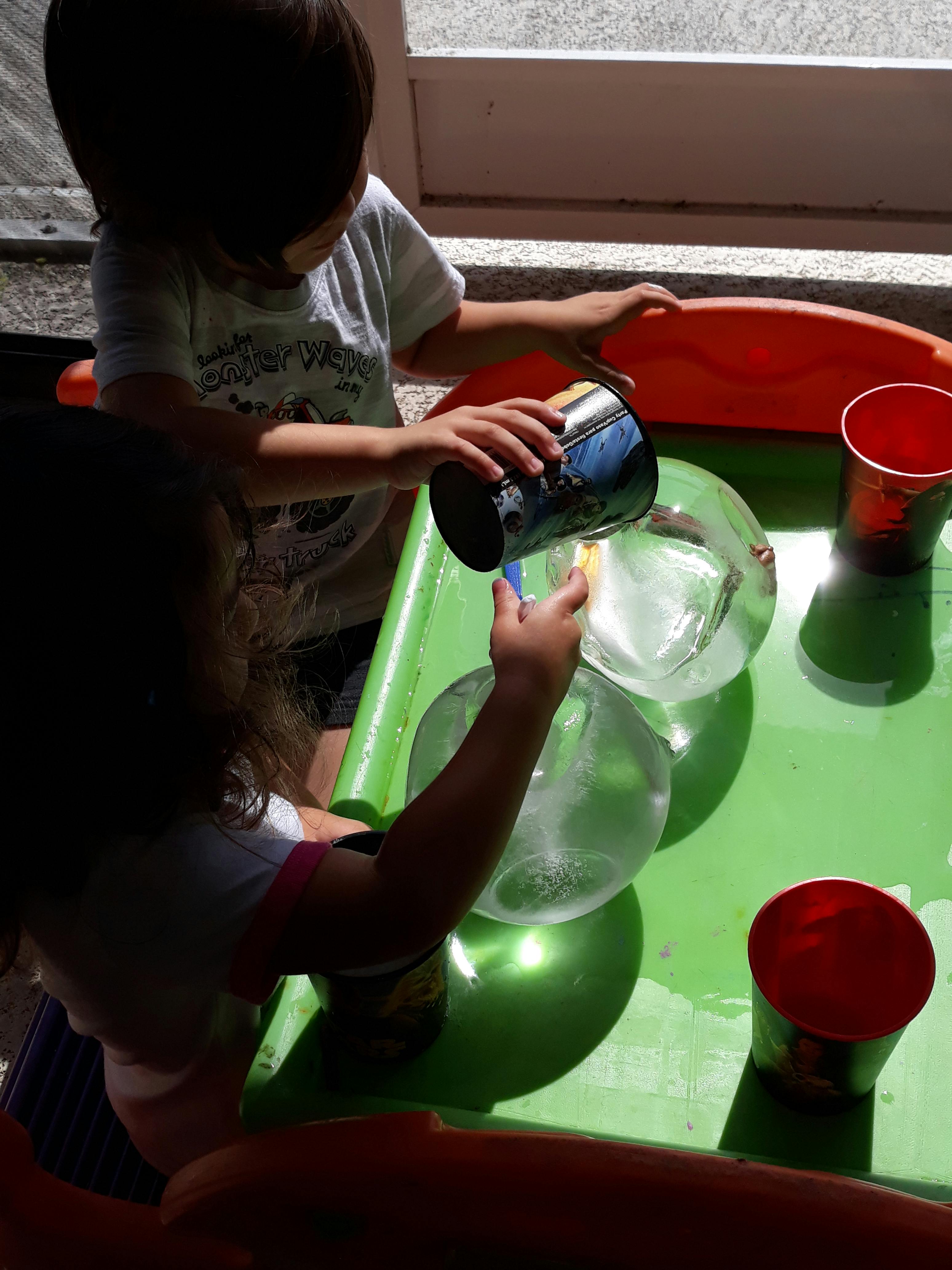 Child pouring water from a cup into a clear bowl on a green table