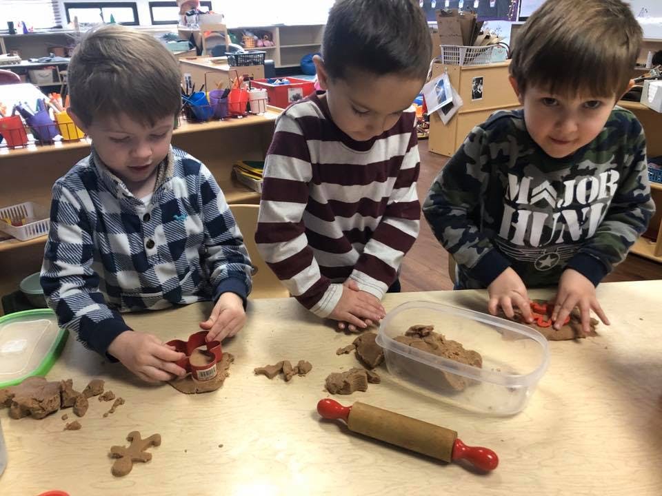 Three children playing with dough and cookie cutters in a classroom