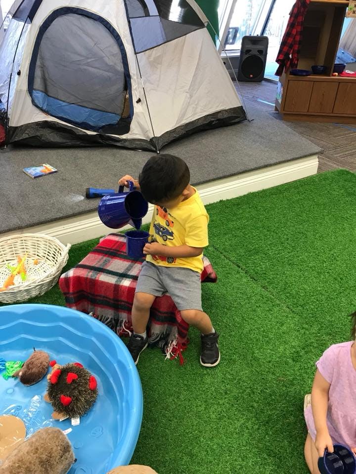 Child pouring water from a blue pitcher into a cup next to a tent