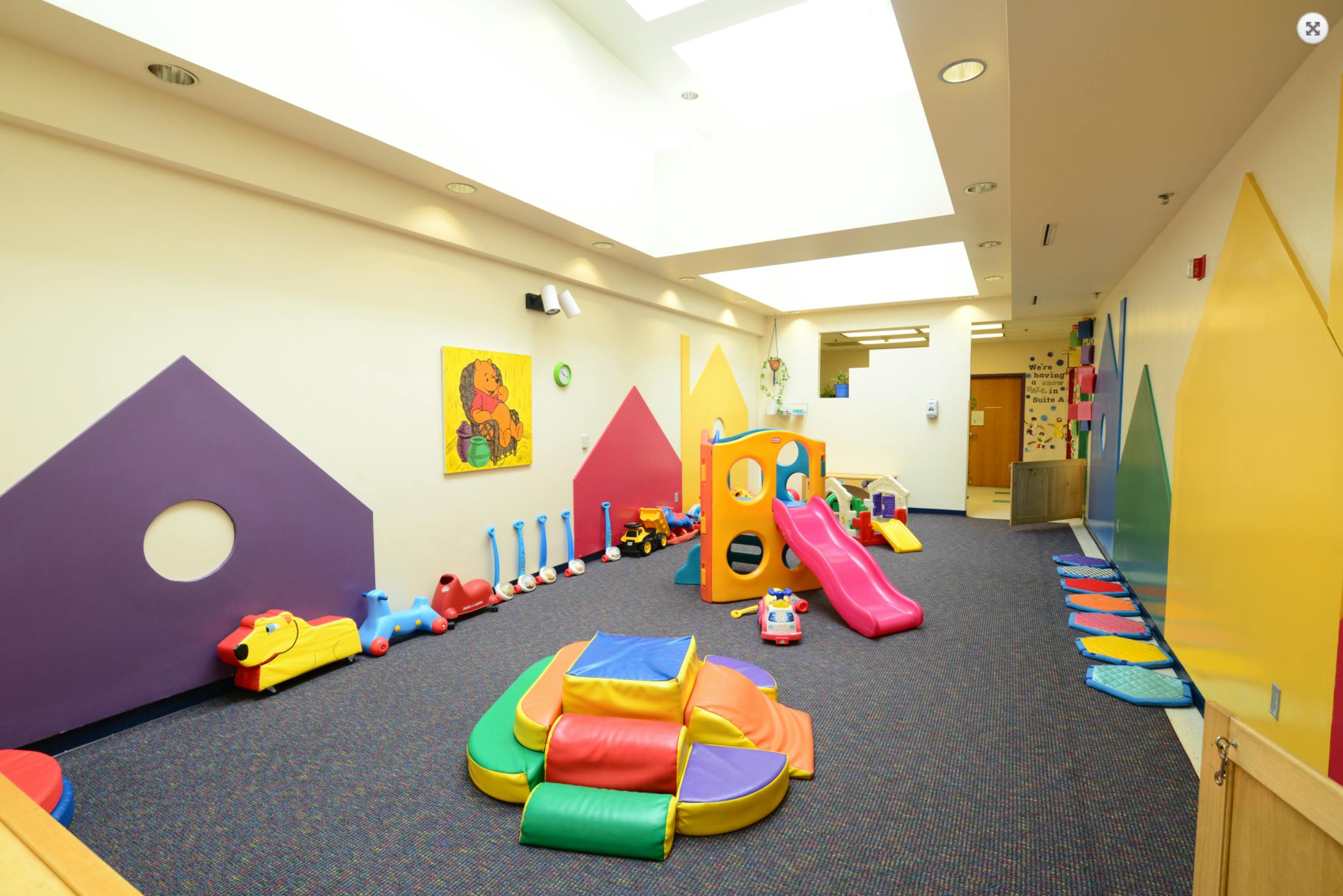 Indoor play area with colorful soft play equipment and a pink slide