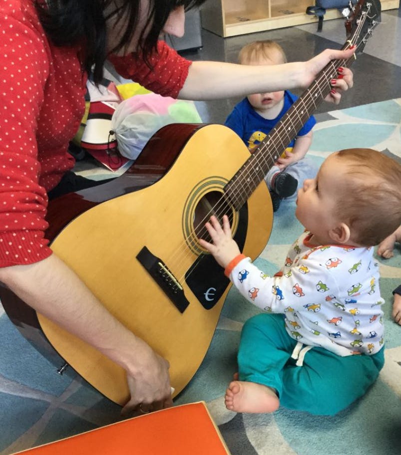Person holding a guitar while a child touches the strings