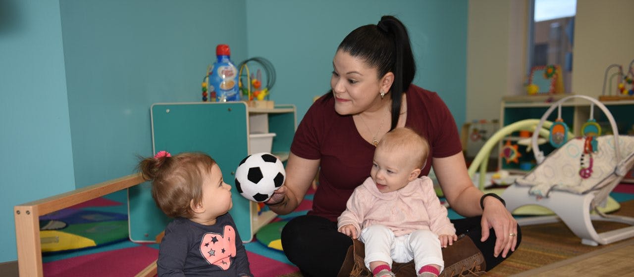 Person holding a soccer ball, looking at two children in a classroom