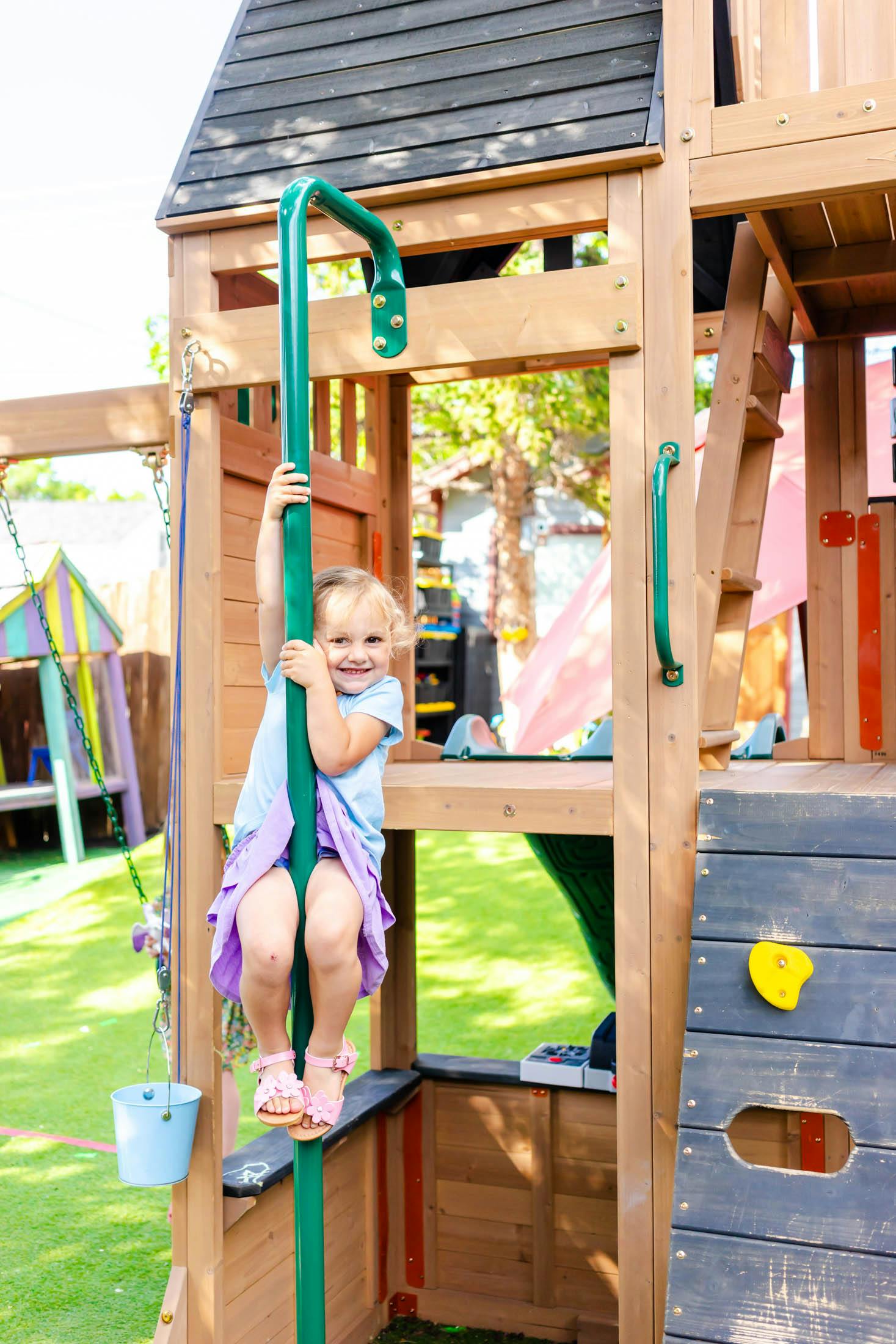 Child on a green fire pole on a wooden playground structure
