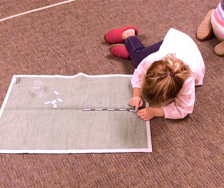 Child lying on floor, working with beads on a mat