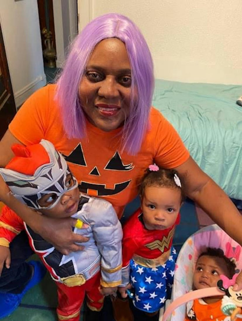 Person in a pumpkin shirt and purple wig with three children in costumes