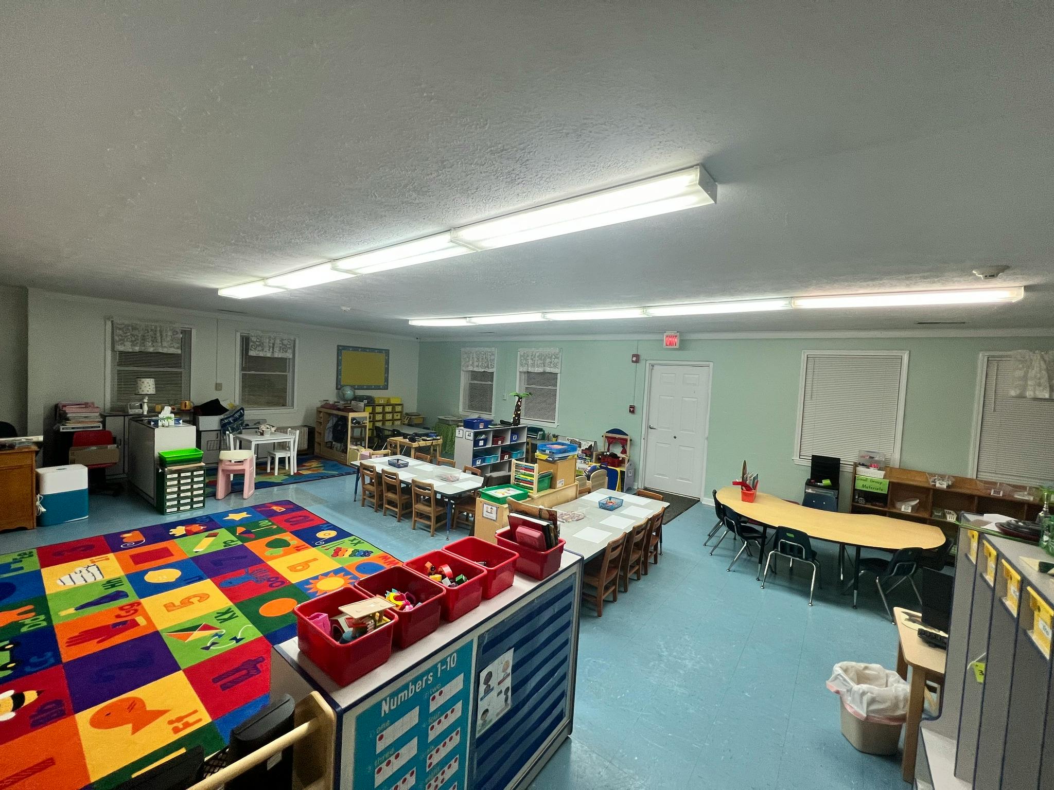 An empty classroom with a colorful alphabet rug, tables, and chairs