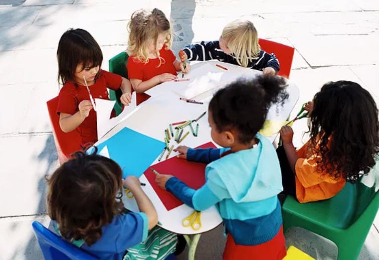 Children sitting around a table doing crafts with paper and crayons