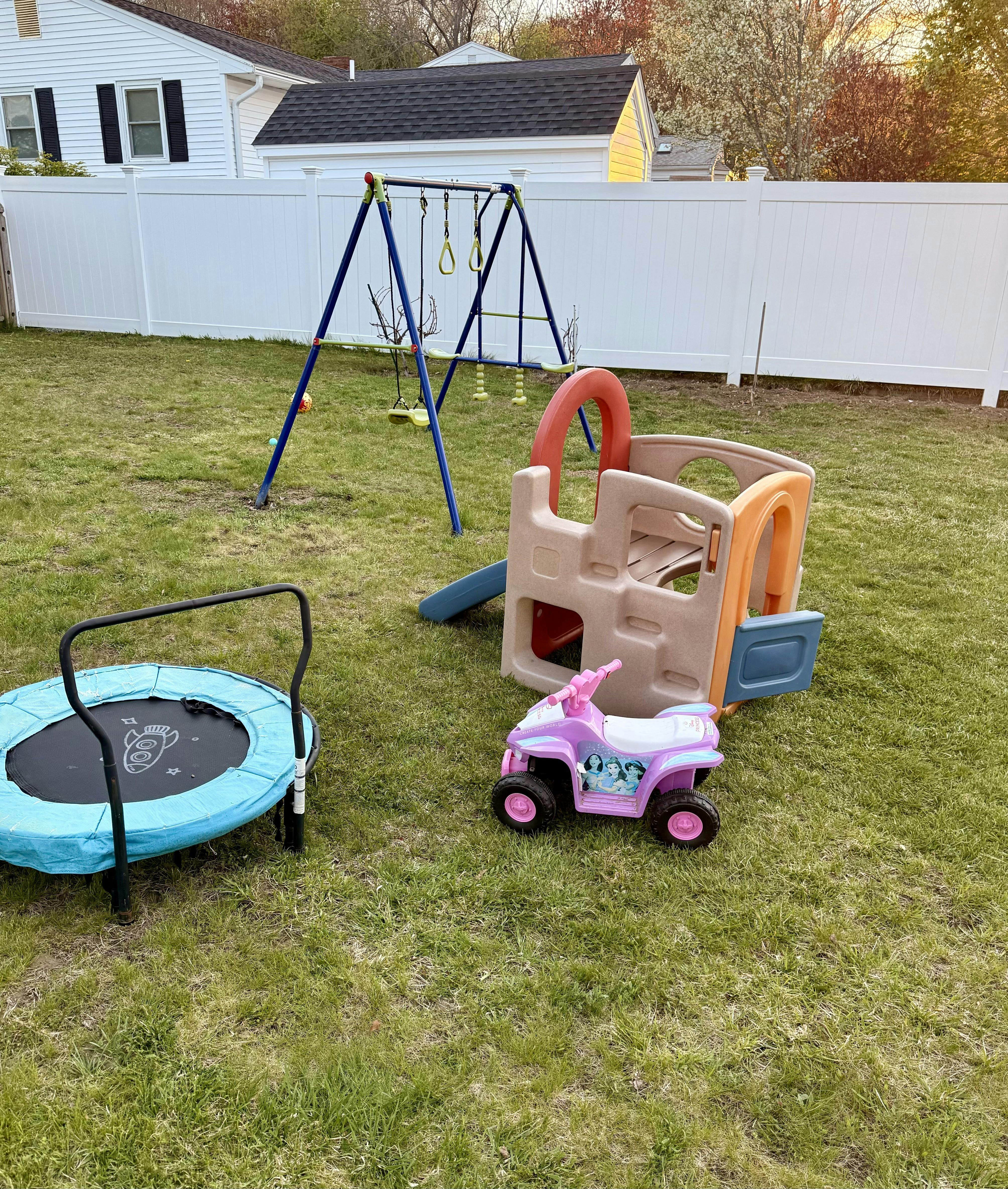 backyard playground with a blue swing set, small slide, and a pink toy ATV
