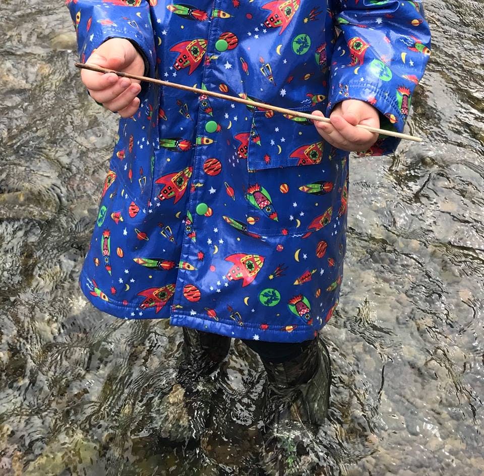 Child in a blue raincoat holding a stick while standing in water