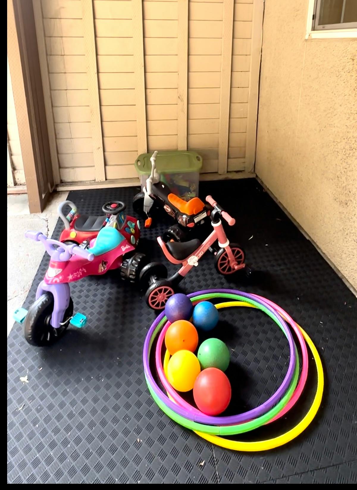 Children's tricycles, balance bike, hula hoops, and balls on a mat