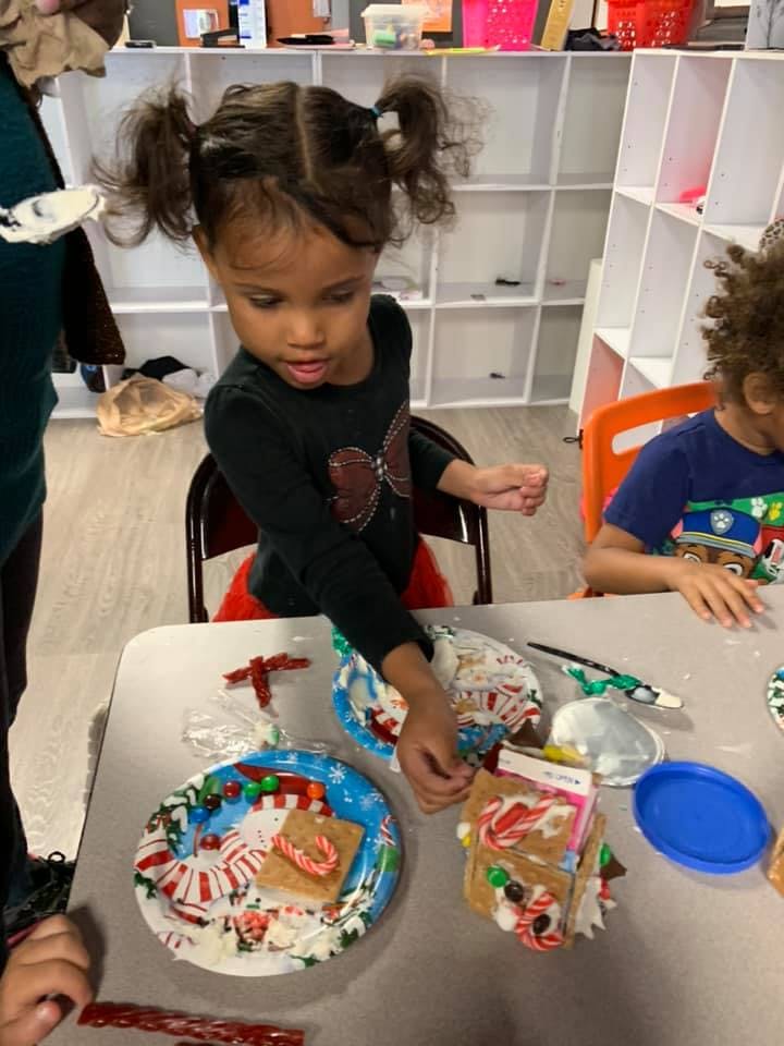 Child decorating a gingerbread house at a table