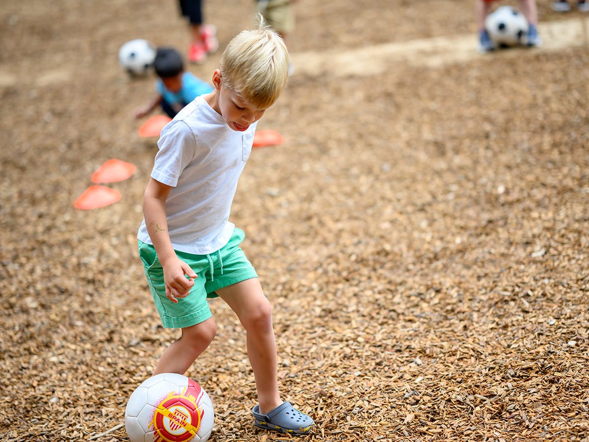 Child playing soccer on wood chips