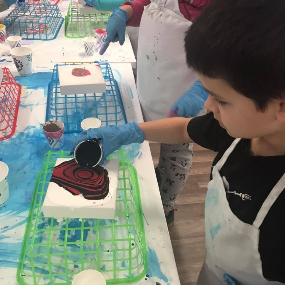 Child in an apron pouring paint onto a canvas
