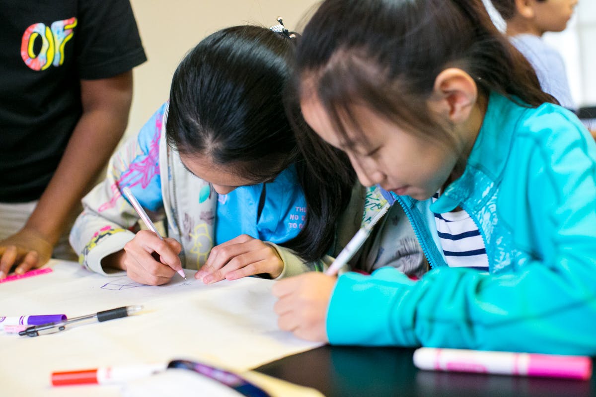 Two children writing on paper at a table