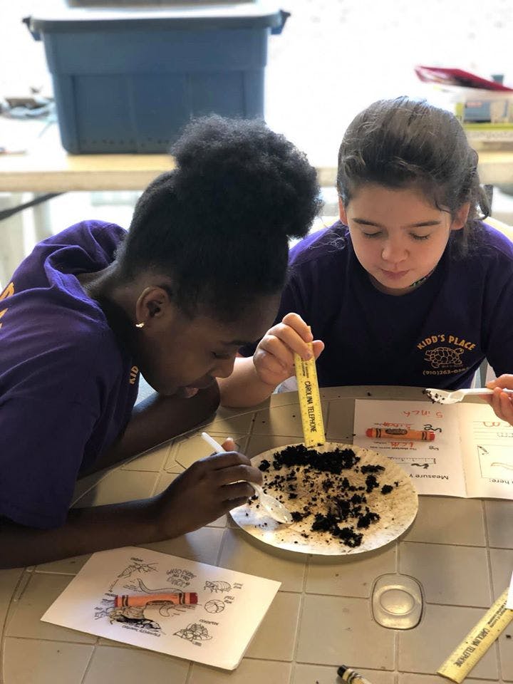 Two children working on a project with dirt on a paper plate