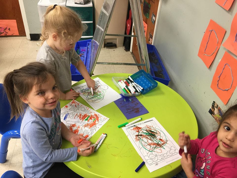 Three children coloring at a green table in a classroom