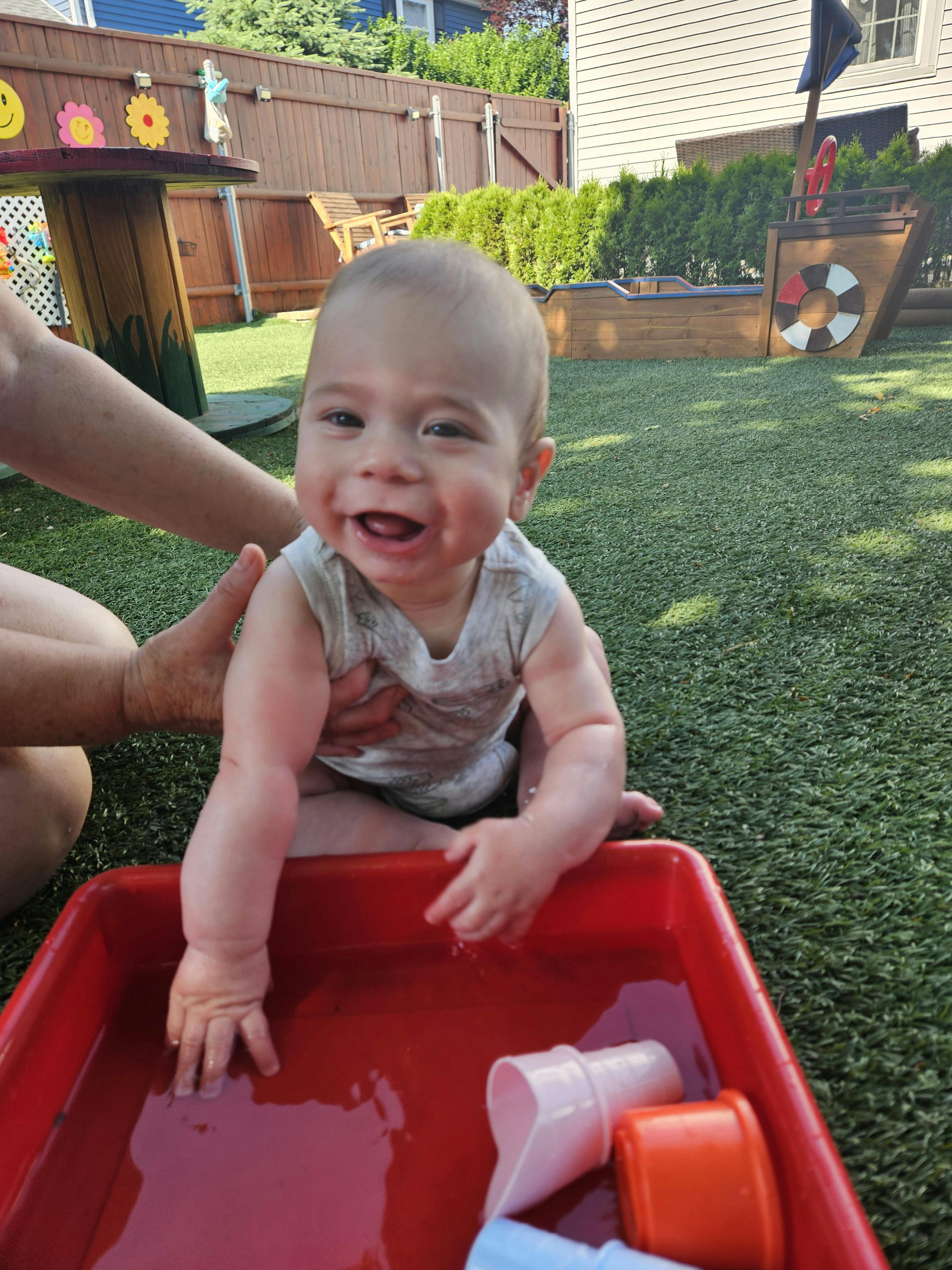 Child playing in a red water bin with toys