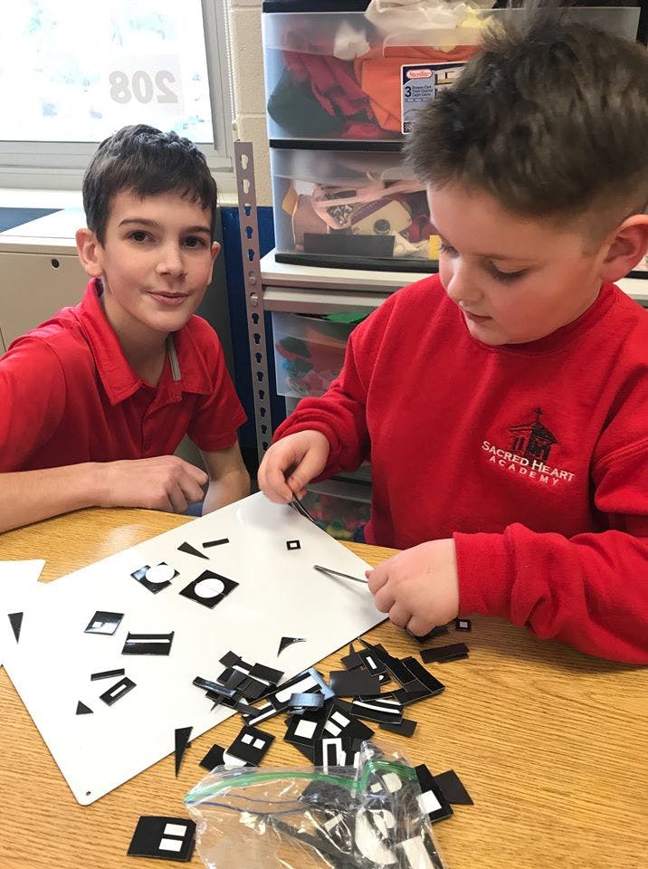Two children working with small black shapes on a white board