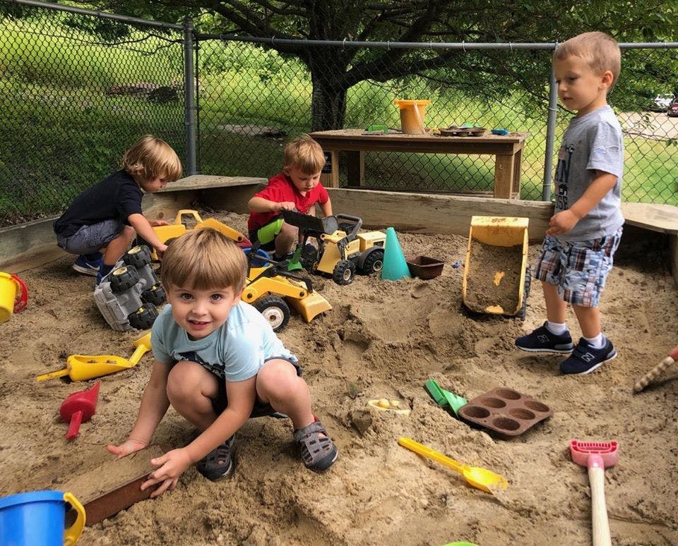 Children playing in a sandbox with toy trucks and shovels