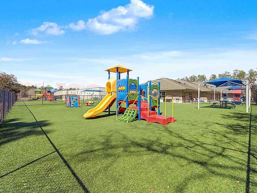 A large playground with multiple colorful play structures and slides on artificial turf