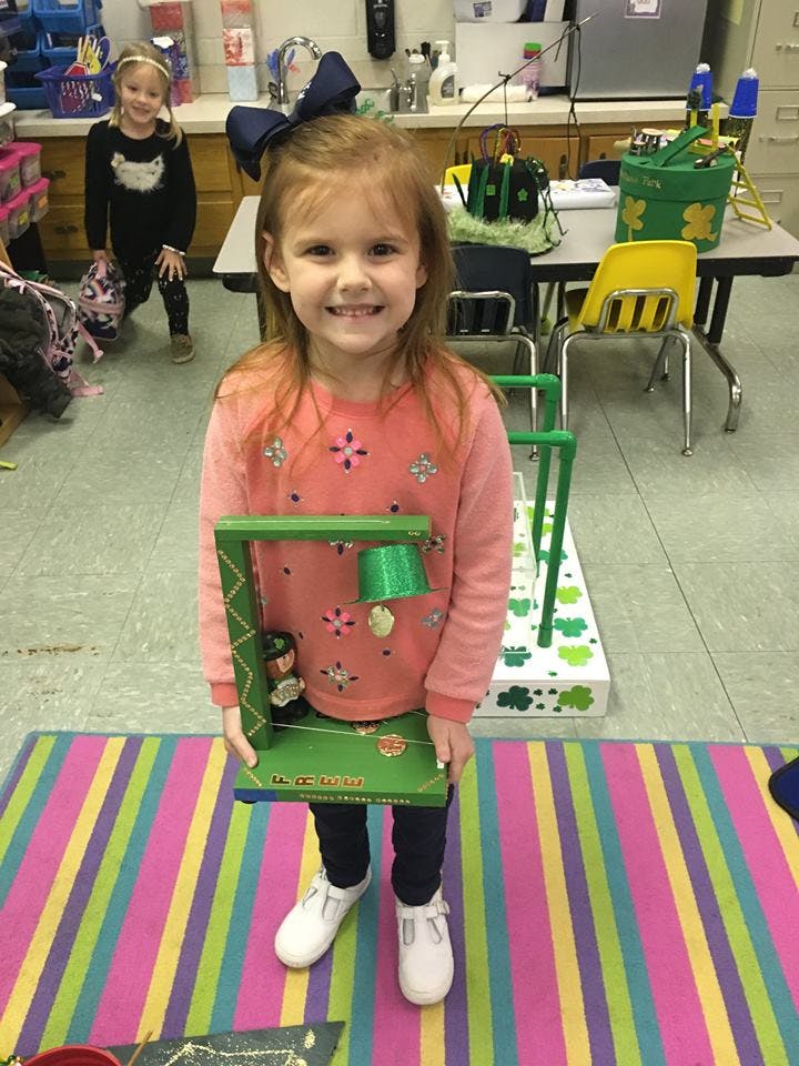 Child holding a green toy with another child in the background