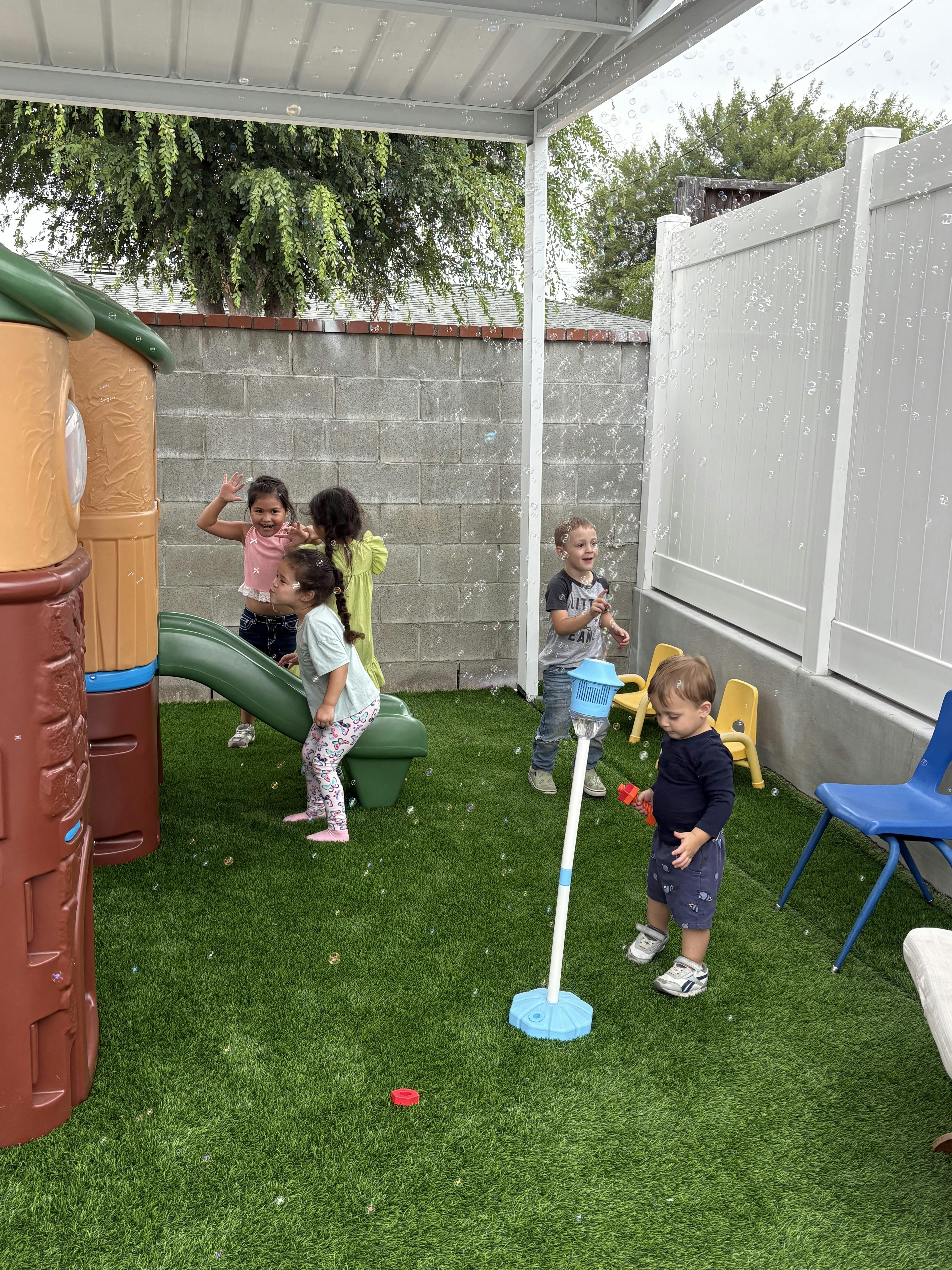 Children playing with a bubble machine in a fenced backyard