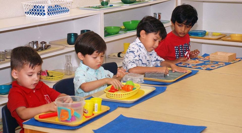 Four children working on individual activities at a table in a classroom