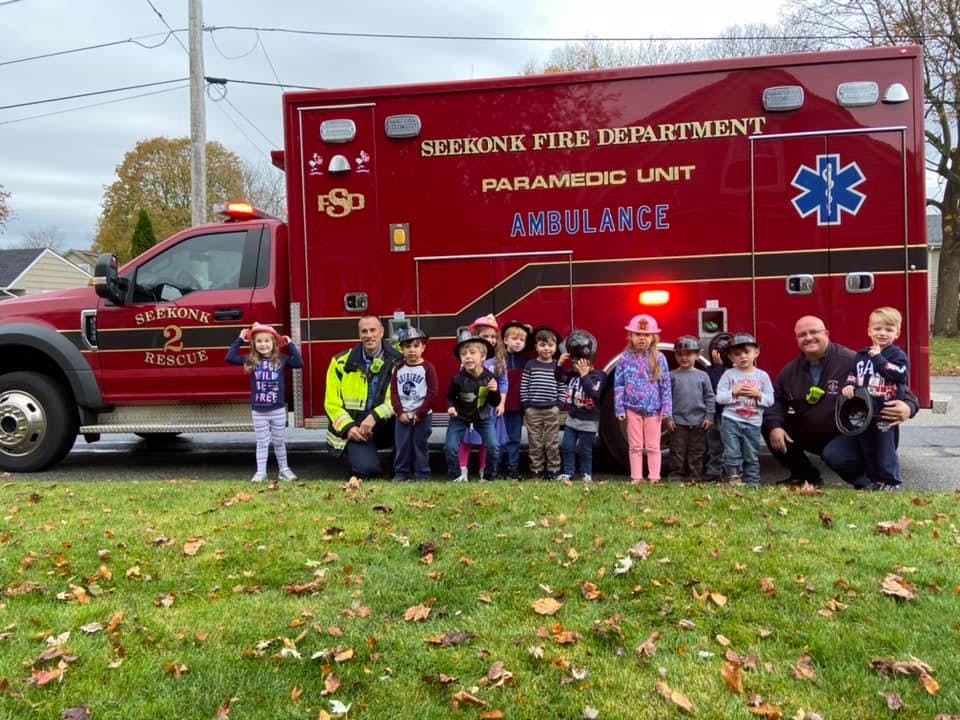 Adults and children standing in front of a red ambulance