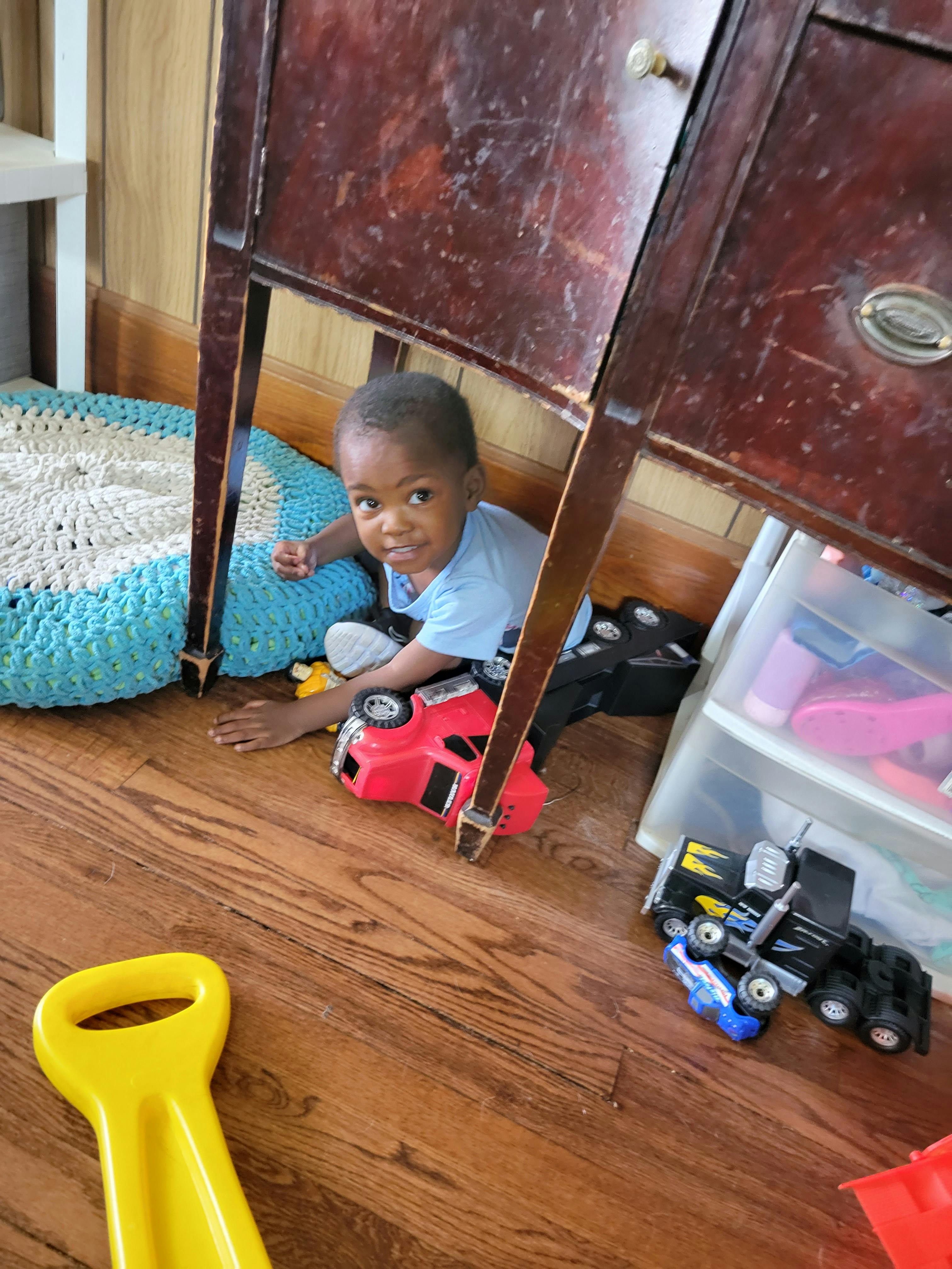 Child playing with a red toy car under a wooden table
