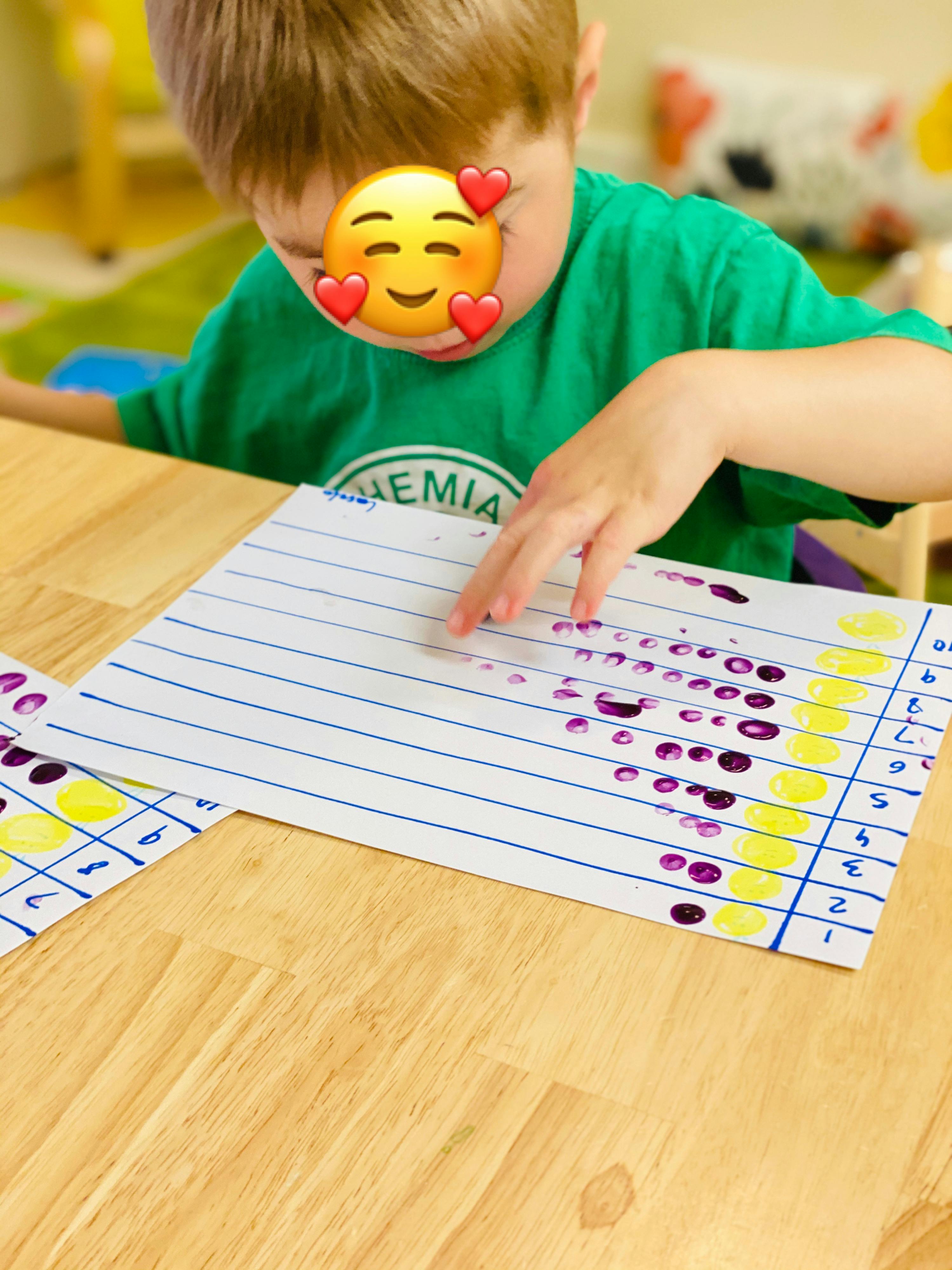 Child's hand touching a paper with purple dots on a wooden table