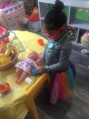 Child wearing red glasses and a stethoscope playing with a doll