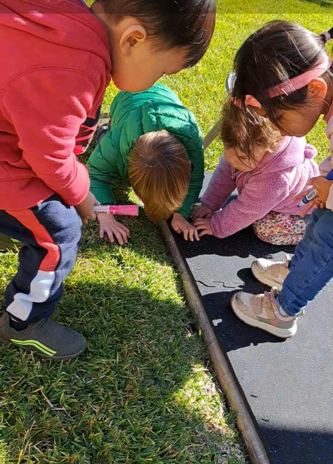Three children looking down at a black mat on the ground
