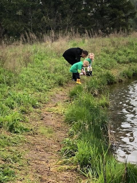 Person and two children looking into water from a grassy bank