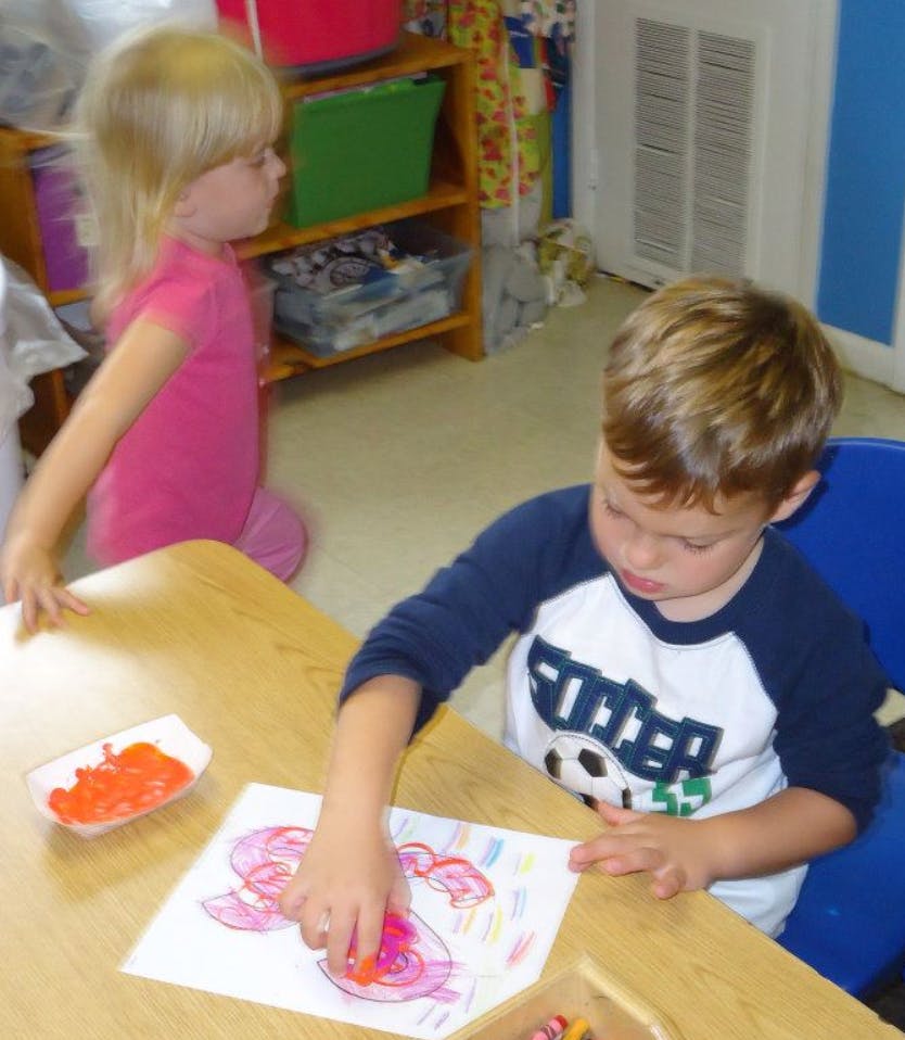 Child finger painting at a table with another child standing nearby