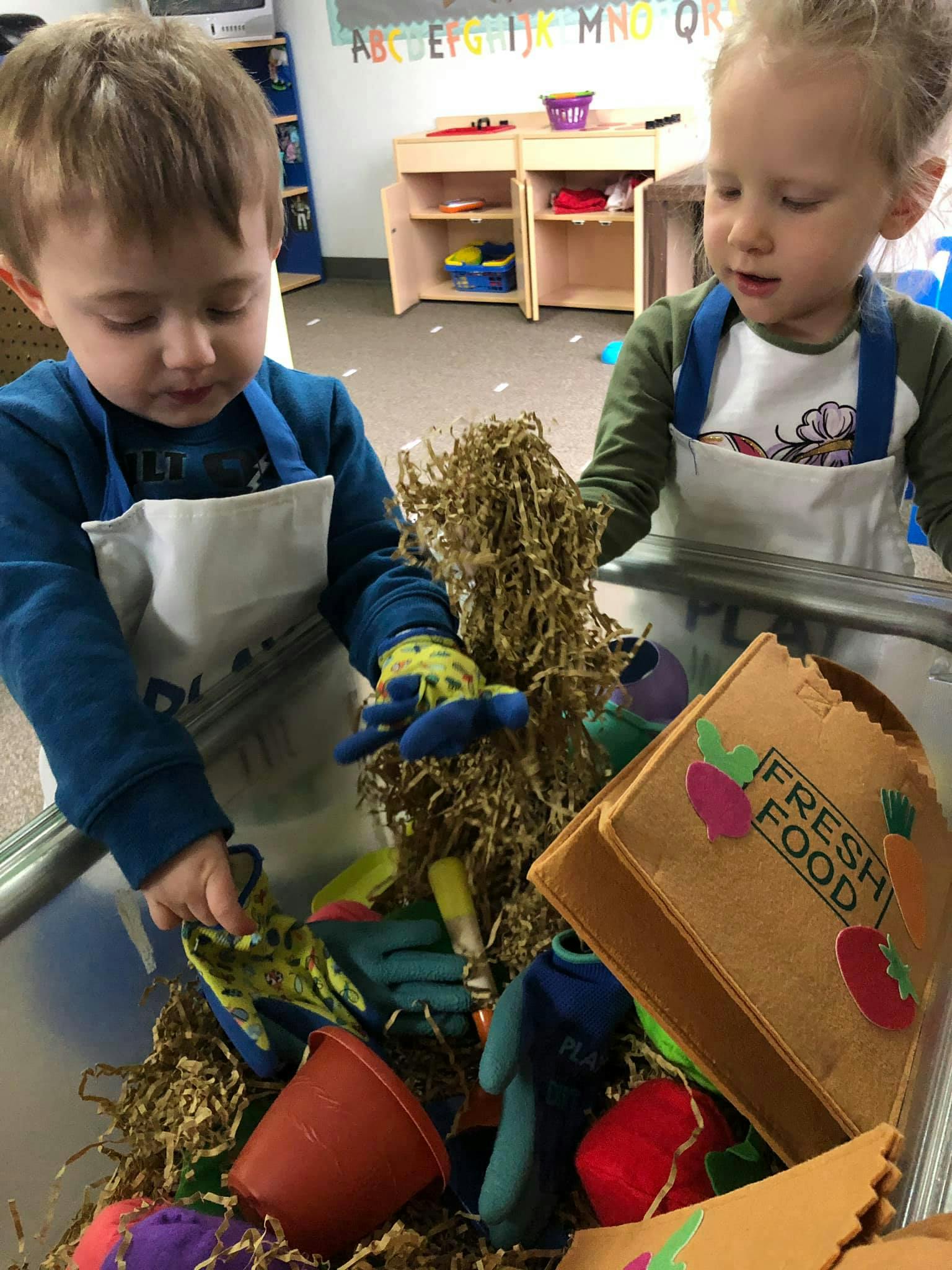 Two children playing with toys and shredded paper in a bin