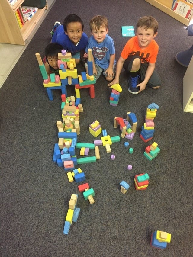 Three children playing with colorful building blocks on the floor