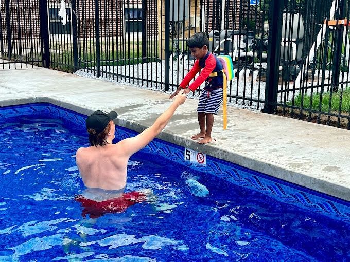 Person in a pool reaching for a child on the pool deck wearing a flotation device