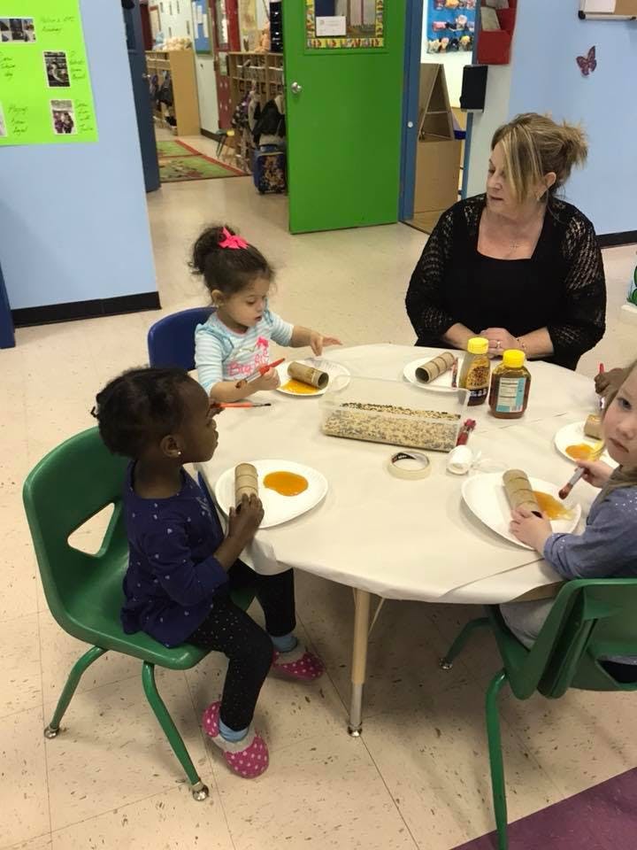 Adult and children at a table doing an art activity with paper towel rolls and paint