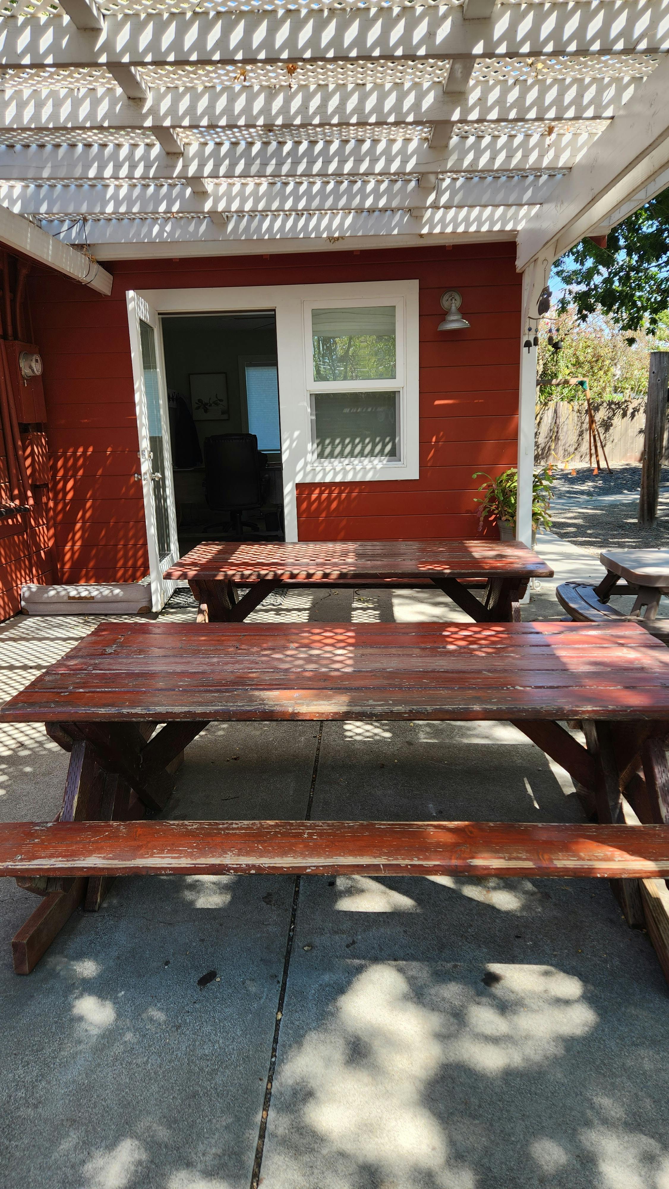 Two picnic tables under a white pergola next to a red building