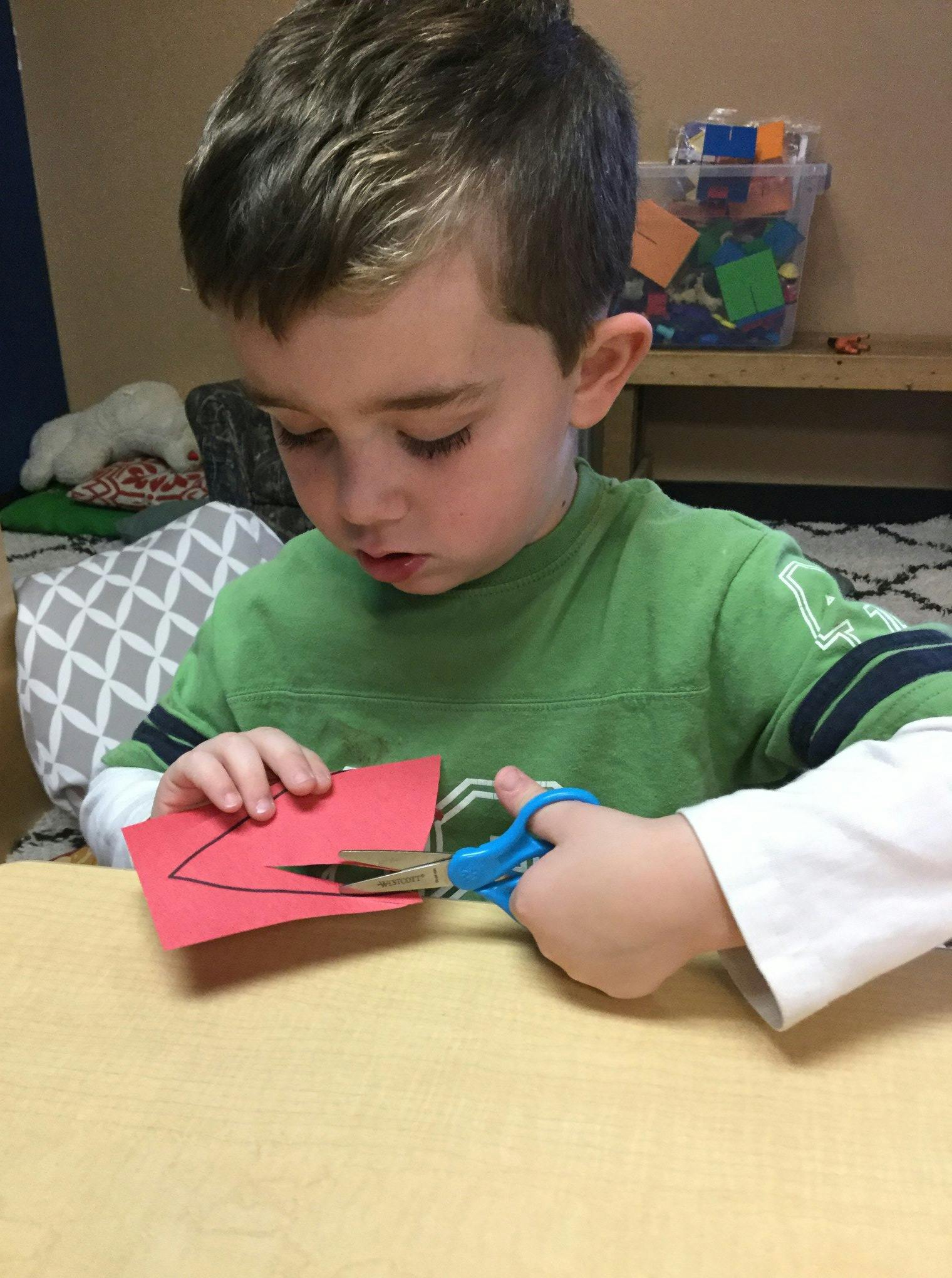 Child cutting red paper with blue scissors