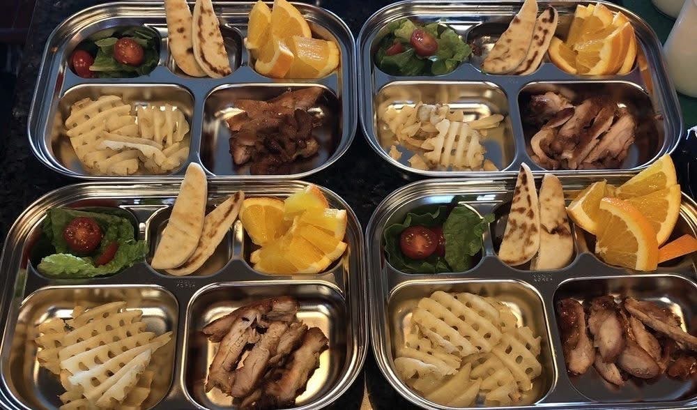 Four metal trays with compartments of food including waffle fries, meat, and fruit